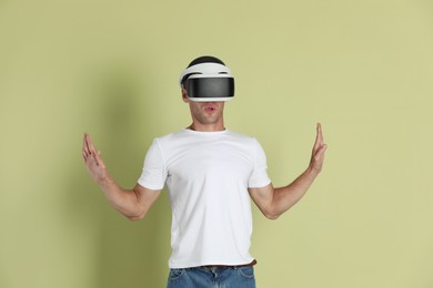 Photo of Surprised man using virtual reality headset on light green background