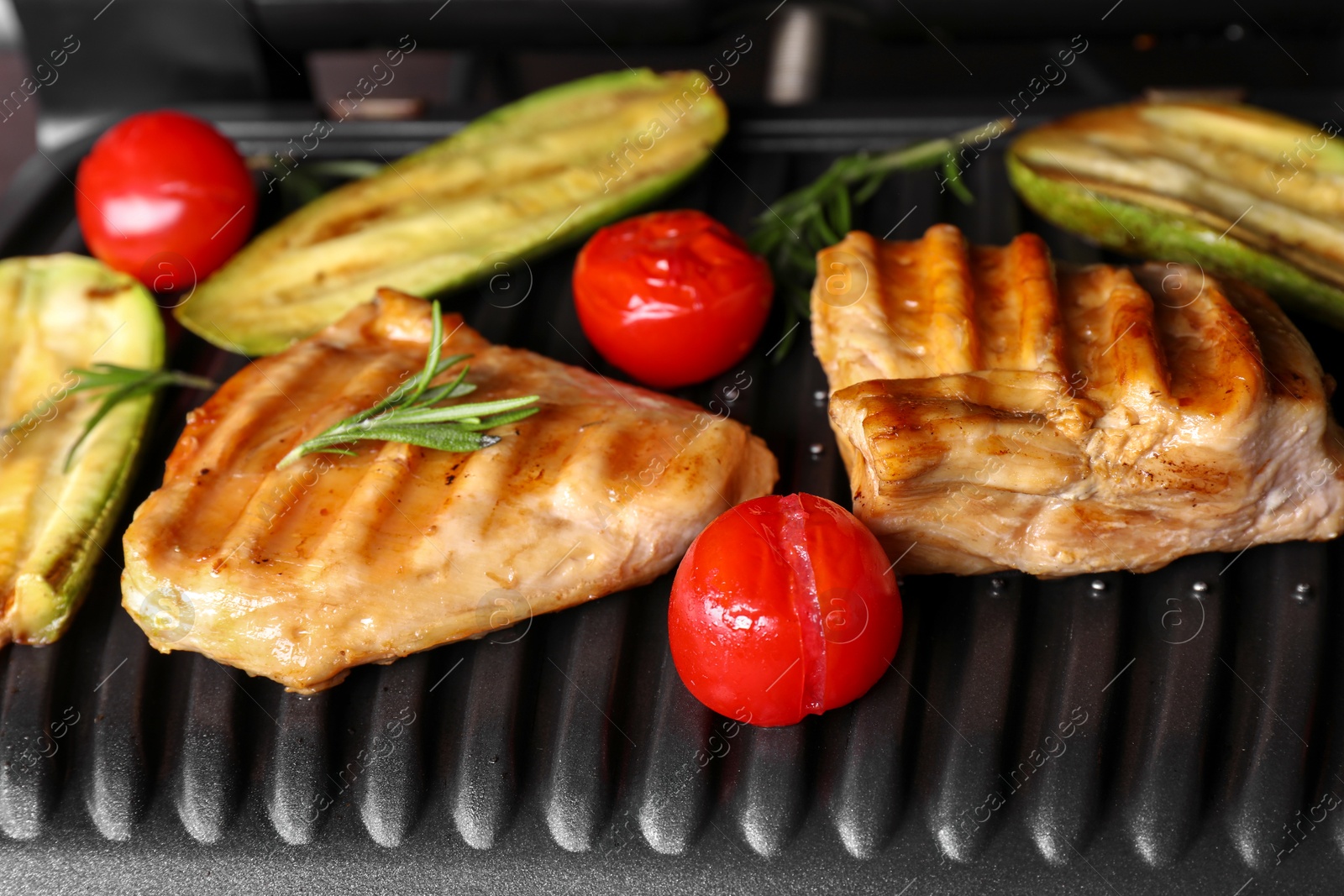 Photo of Tasty meat, rosemary and vegetables on electric grill, closeup