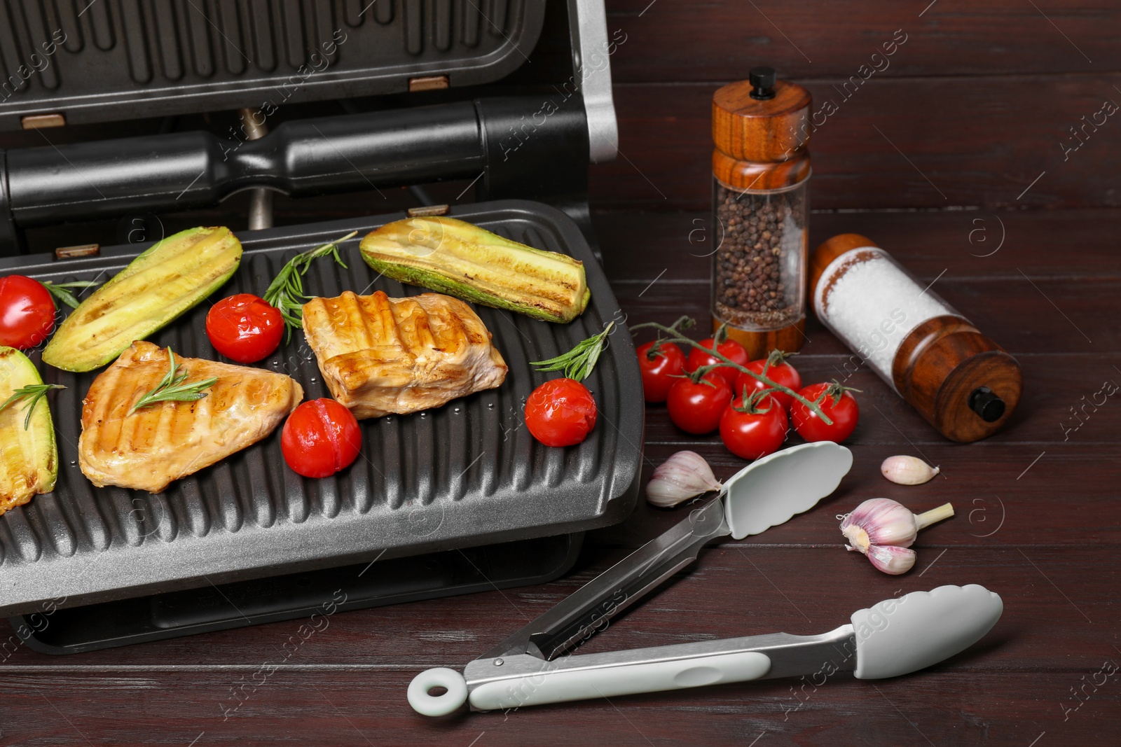 Photo of Electric grill with tasty meat, spices and vegetables on wooden table