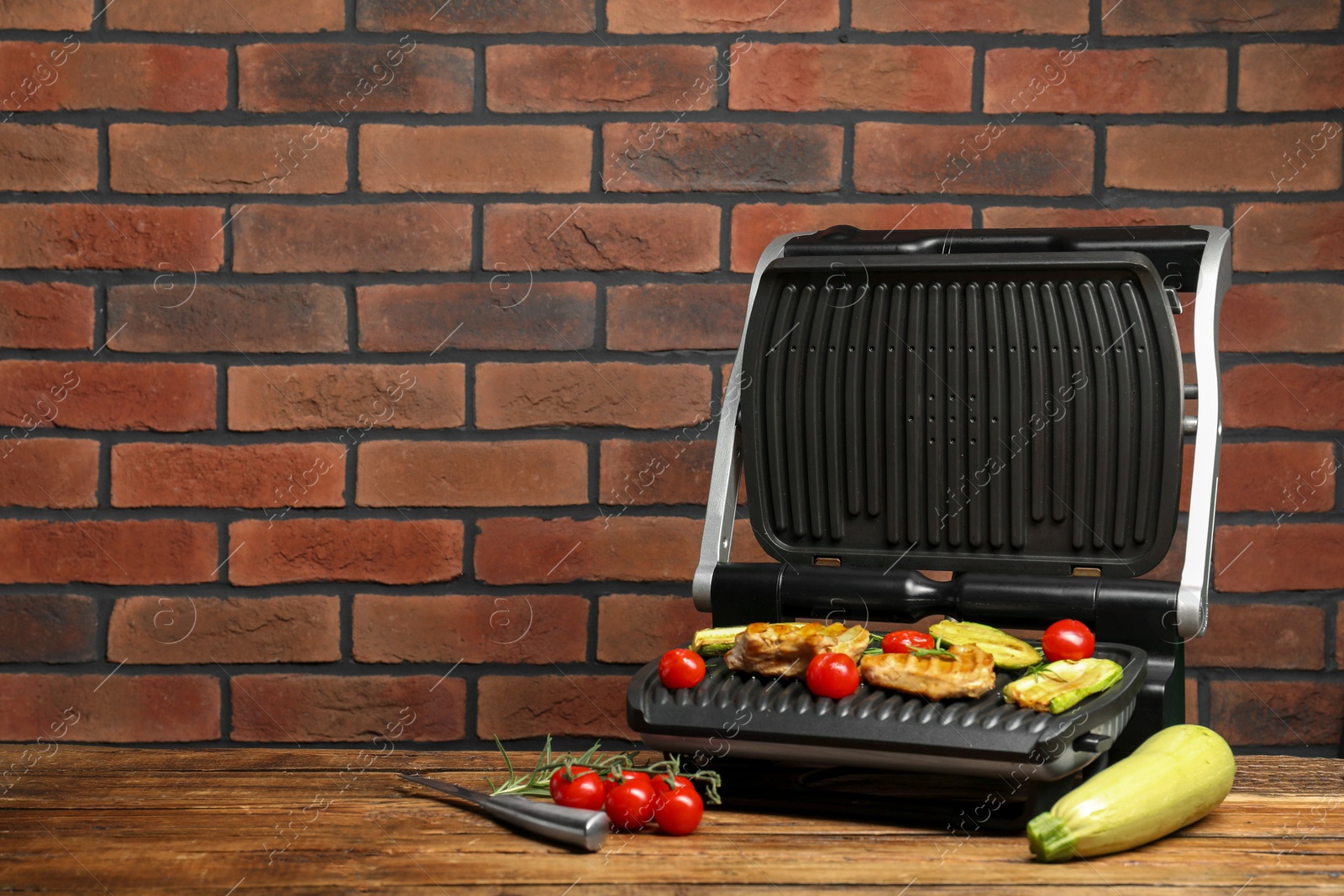 Photo of Electric grill with tasty meat, rosemary and vegetables on wooden table, space for text