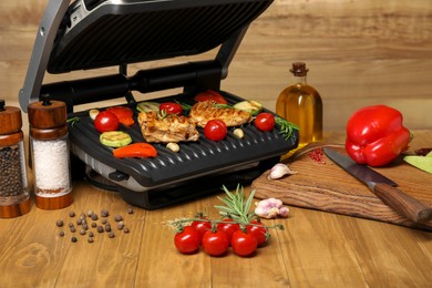 Electric grill with different products and knife on wooden table