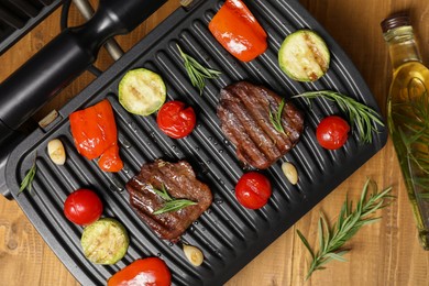 Photo of Electric grill with different products on wooden table, flat lay