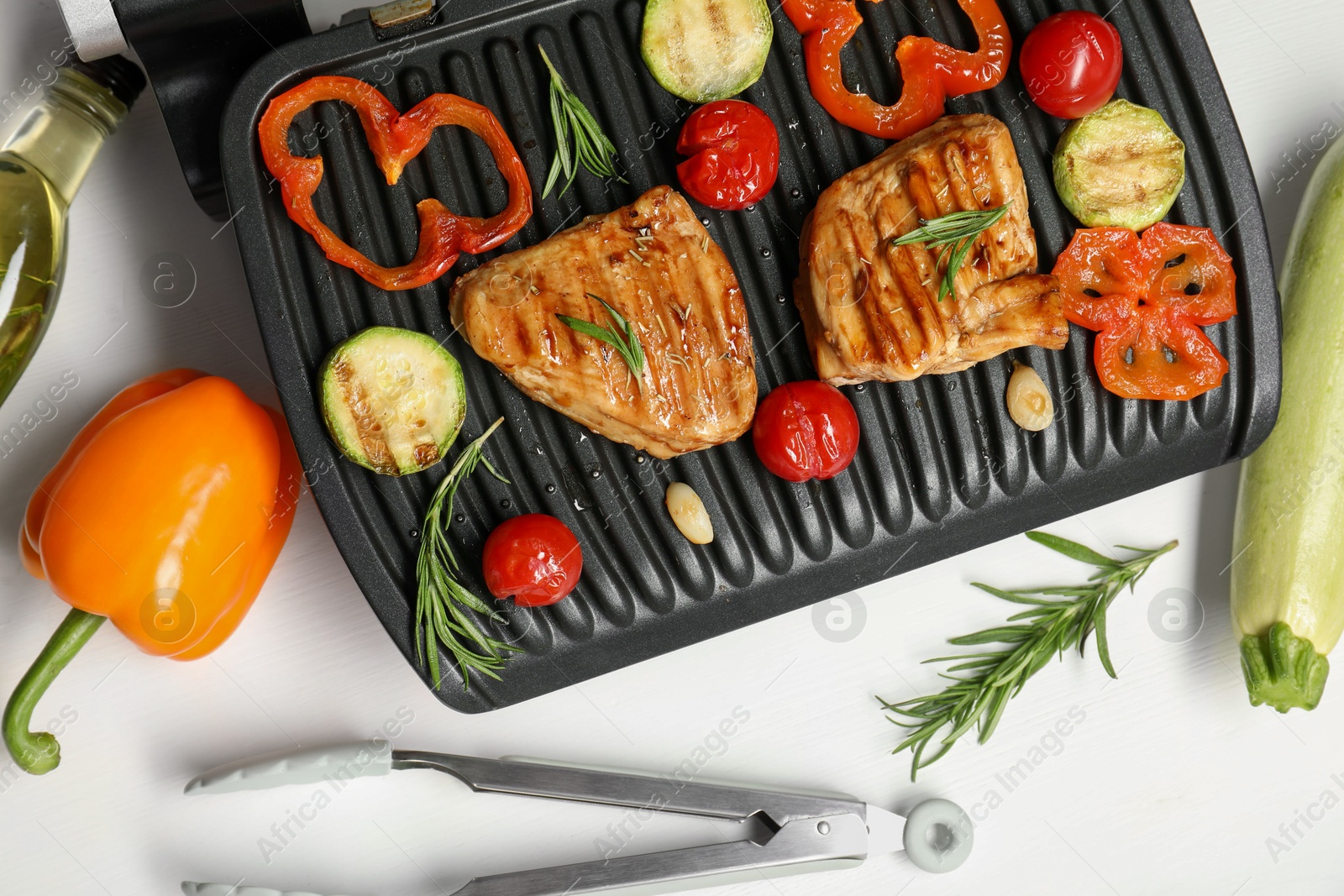 Photo of Electric grill with tasty meat, spices and vegetables on white table, flat lay