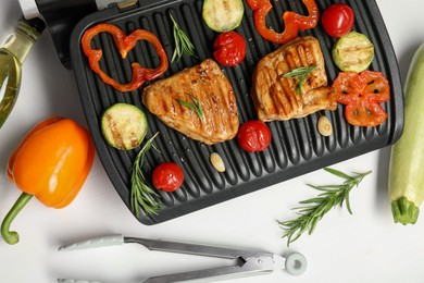 Electric grill with tasty meat, spices and vegetables on white table, flat lay