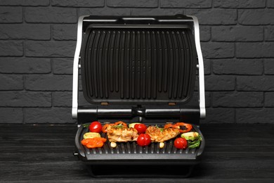 Photo of Electric grill with tasty meat, spices and vegetables on black wooden table