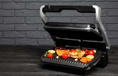 Photo of Electric grill with tasty meat, spices and vegetables on black wooden table