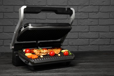 Electric grill with tasty meat, spices and vegetables on black wooden table, space for text