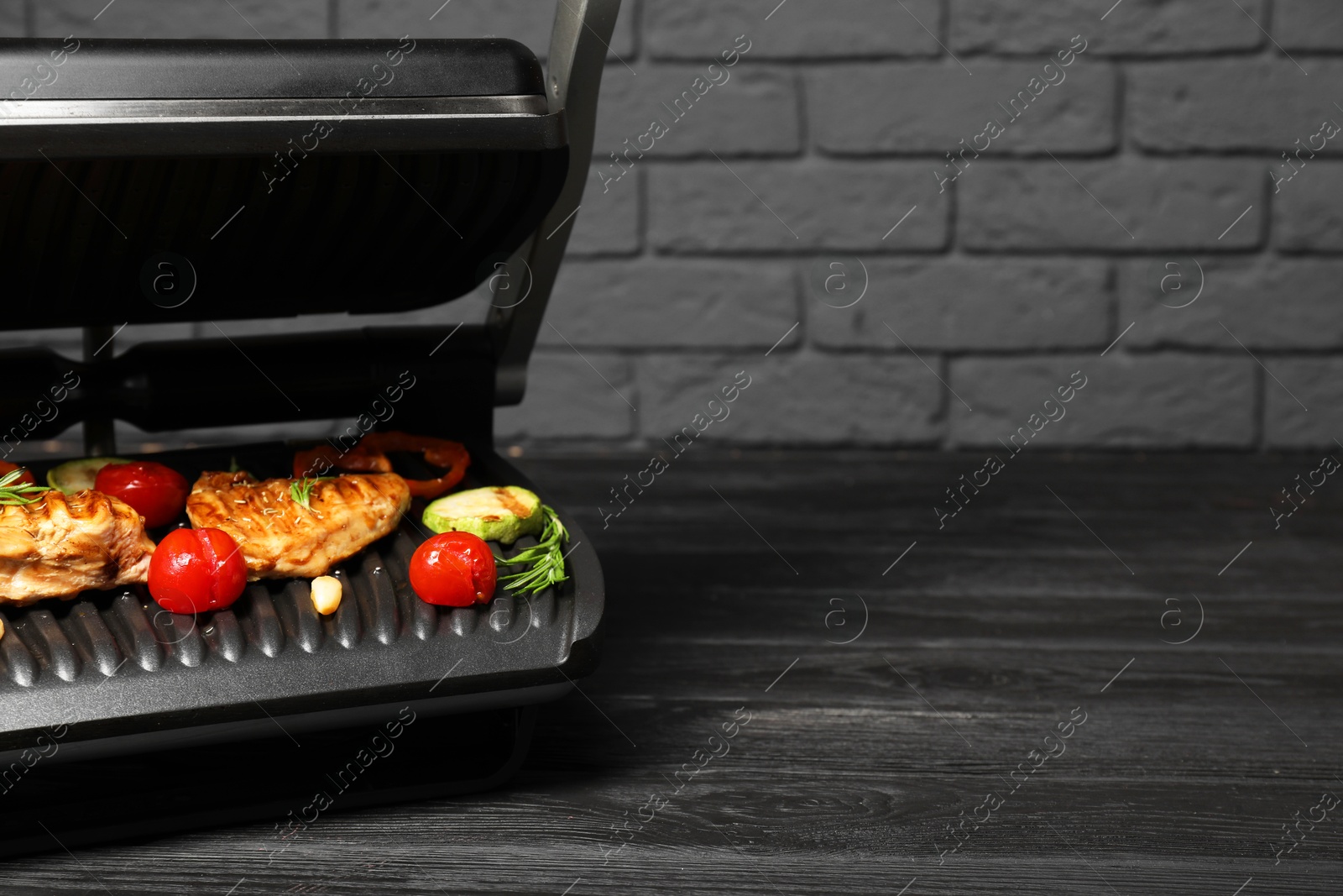 Photo of Electric grill with tasty meat, spices and vegetables on black wooden table, space for text