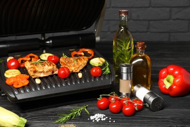 Photo of Electric grill with different products on black wooden table