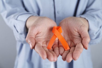Woman with orange awareness ribbon on grey background, closeup