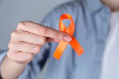Woman with orange awareness ribbon on grey background, closeup