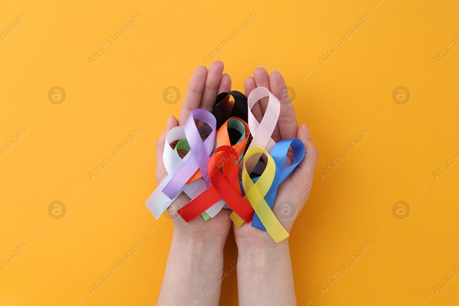 Photo of Woman with many colorful awareness ribbons on orange background, top view