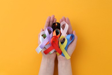 Photo of Woman with many colorful awareness ribbons on orange background, top view