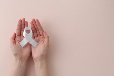 Photo of Woman with white awareness ribbon on beige background, top view. Space for text