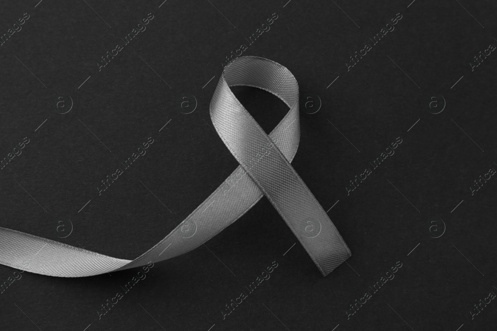 Photo of Grey awareness ribbon on black background, top view