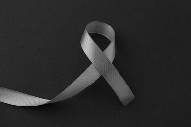 Photo of Grey awareness ribbon on black background, top view