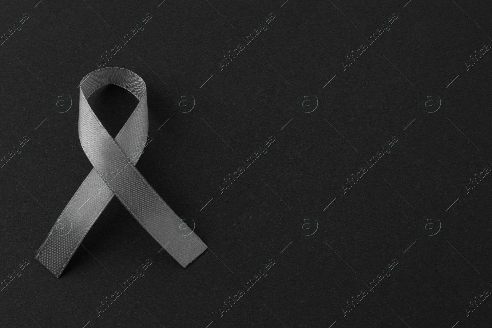 Photo of Grey awareness ribbon on black background, top view. Space for text