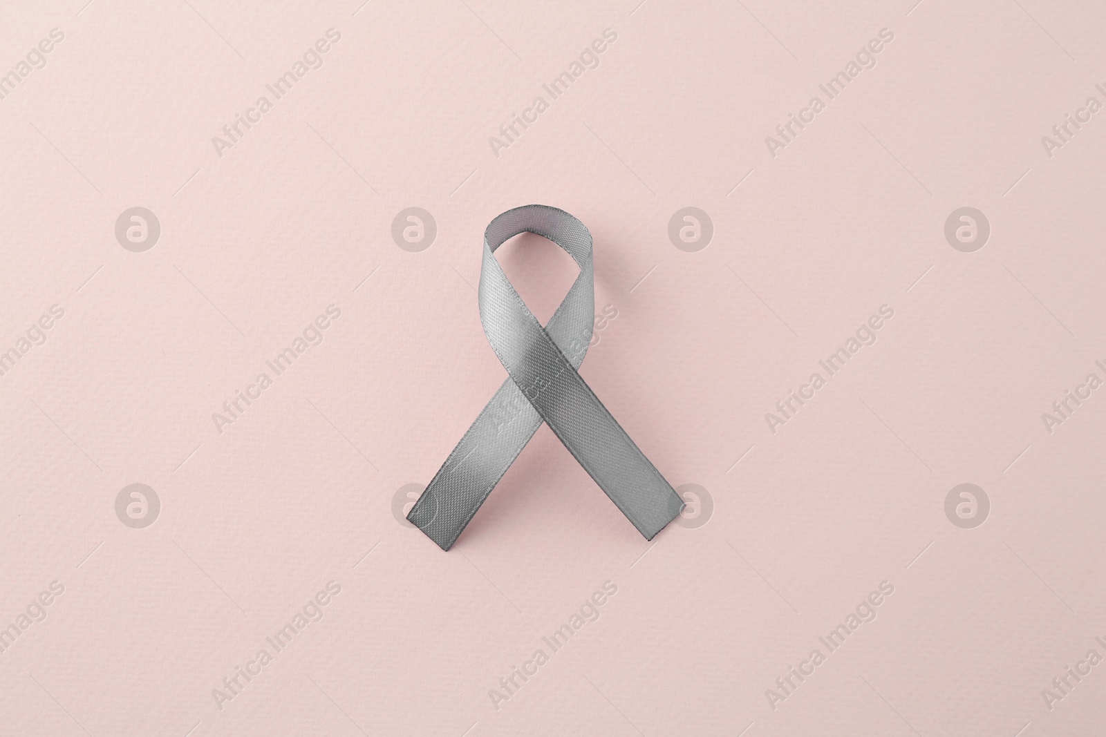 Photo of Grey awareness ribbon on beige background, top view