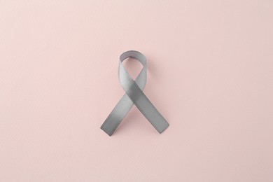 Photo of Grey awareness ribbon on beige background, top view