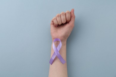 Woman with violet awareness ribbon on light blue background, top view