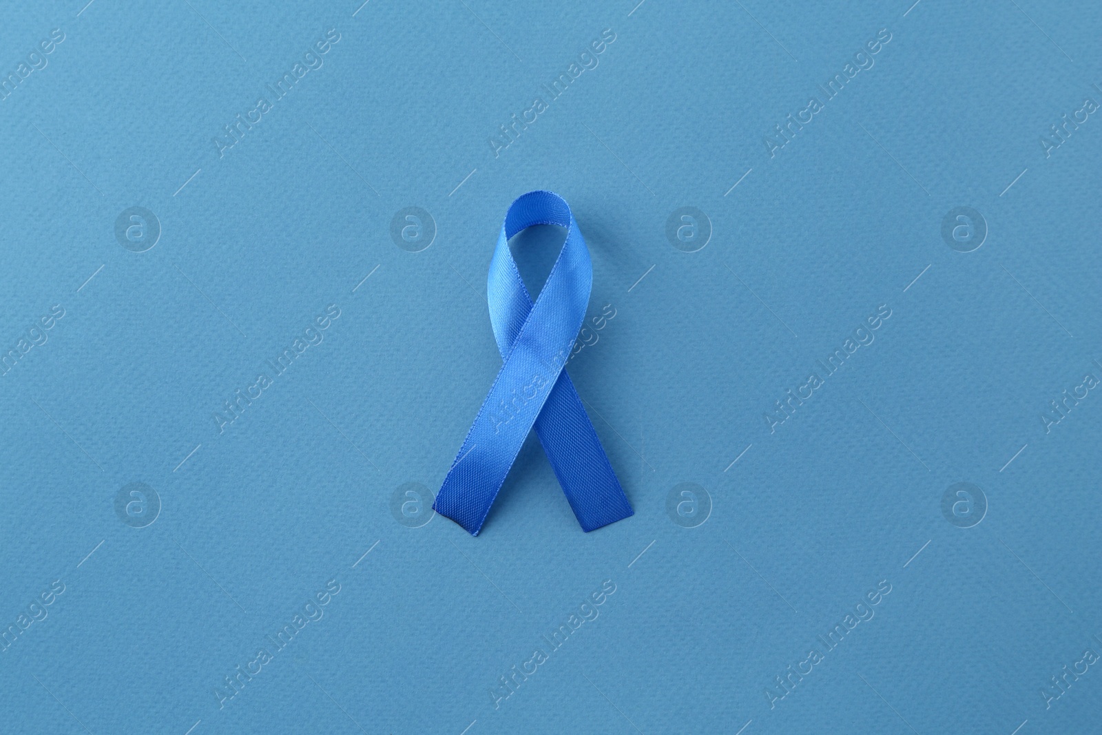 Photo of Blue awareness ribbon on color background, top view