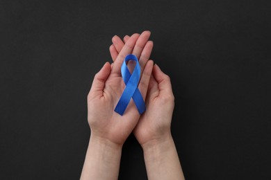 Photo of Woman with blue awareness ribbon on black background, top view