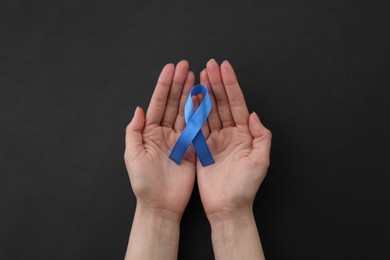 Photo of Woman with blue awareness ribbon on black background, top view