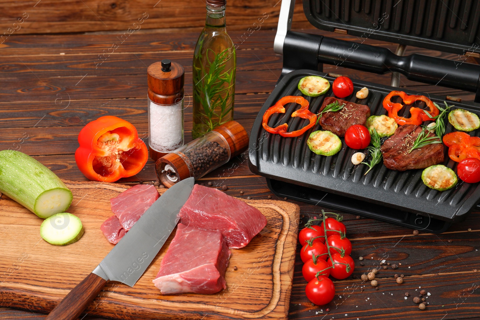 Photo of Electric grill with meat, spices, knife and vegetables on wooden table