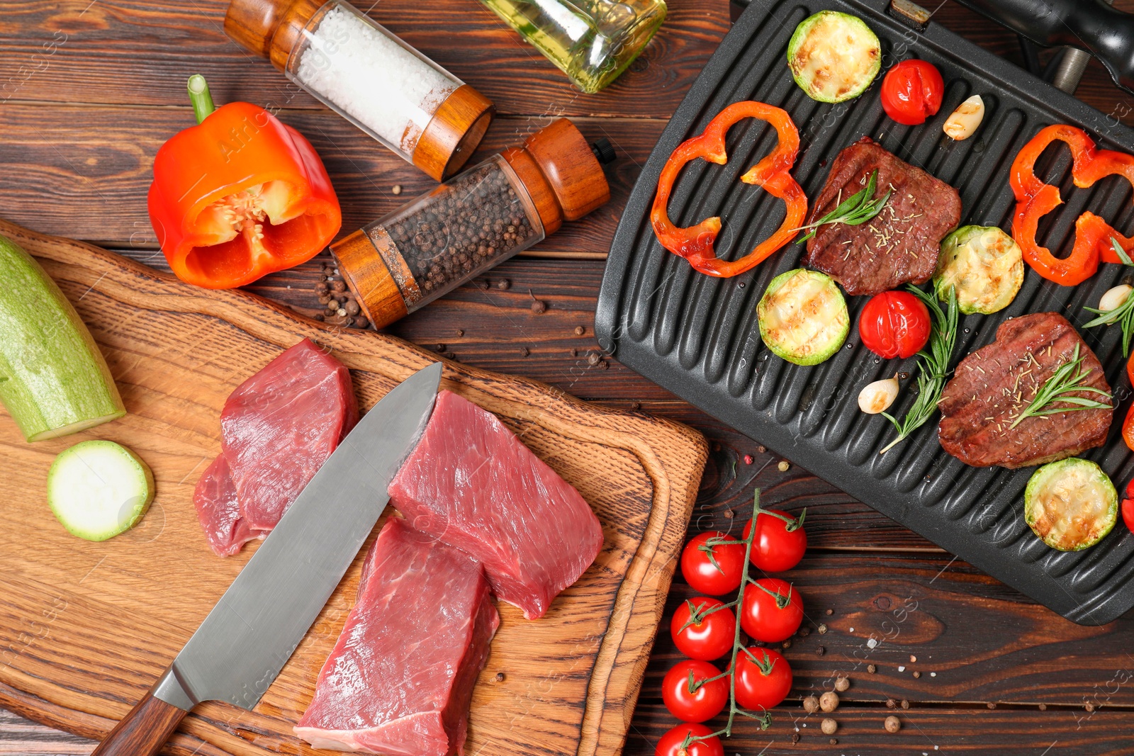 Photo of Electric grill with meat, spices, knife and vegetables on wooden table, flat lay