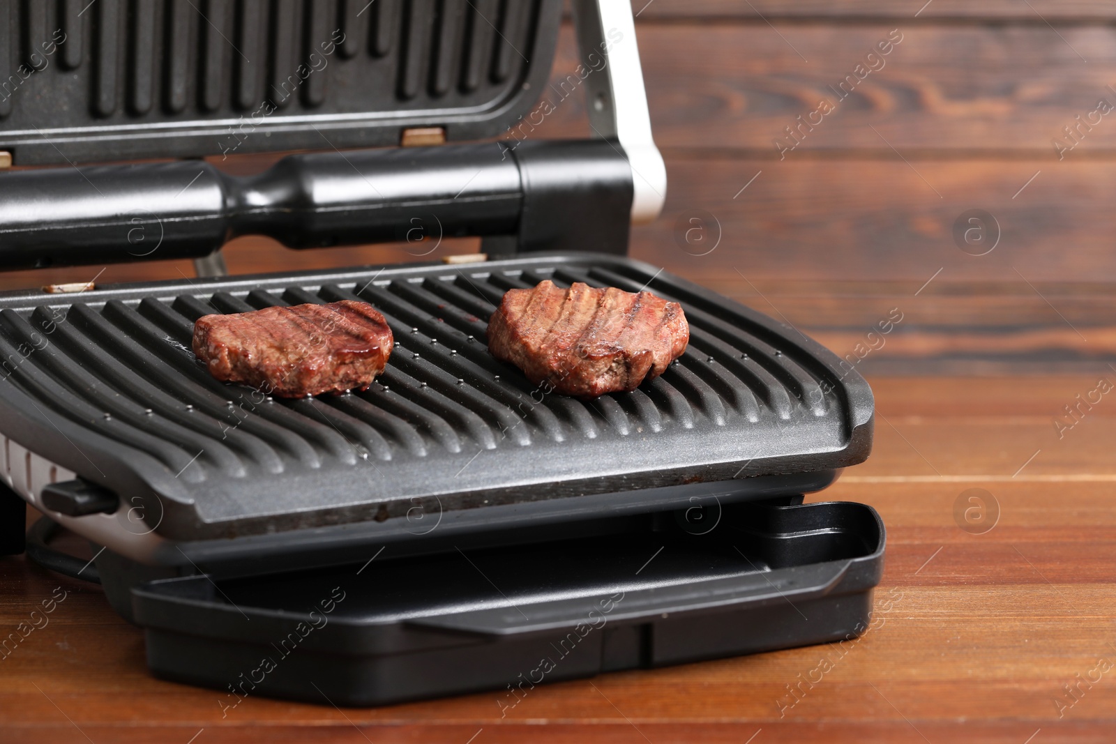 Photo of Electric grill with tasty meat steaks on wooden table, closeup