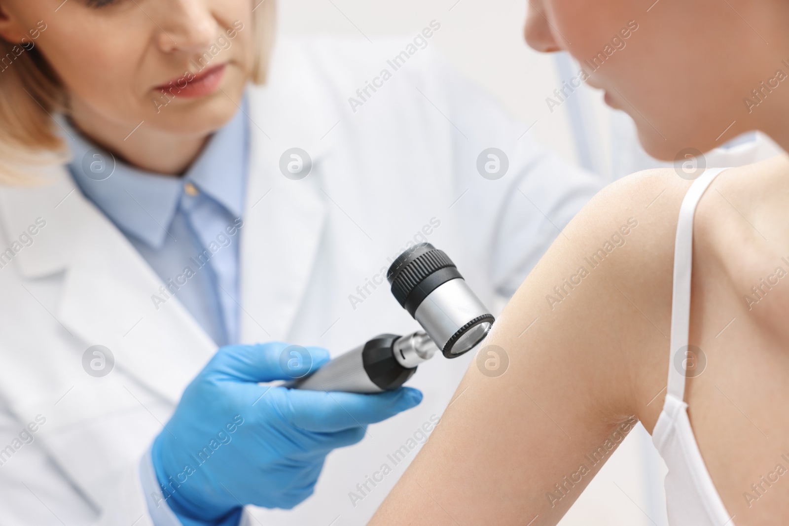 Photo of Dermatologist with dermatoscope examining patient in clinic, closeup