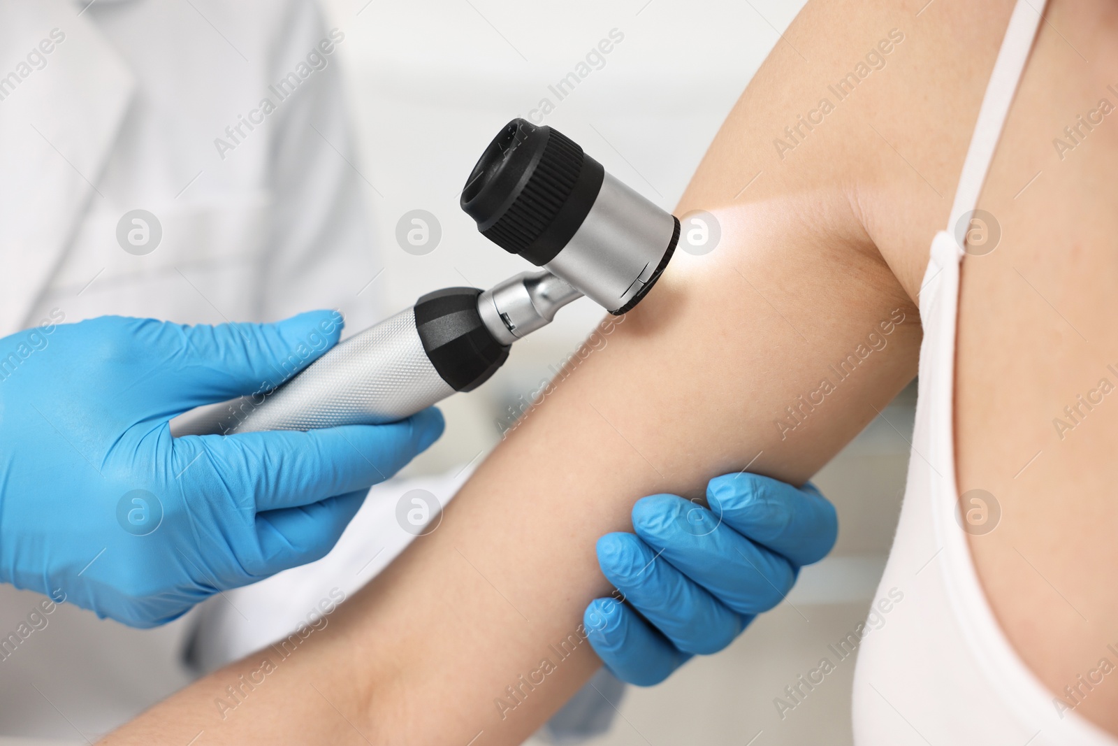 Photo of Dermatologist with dermatoscope examining patient in clinic, closeup