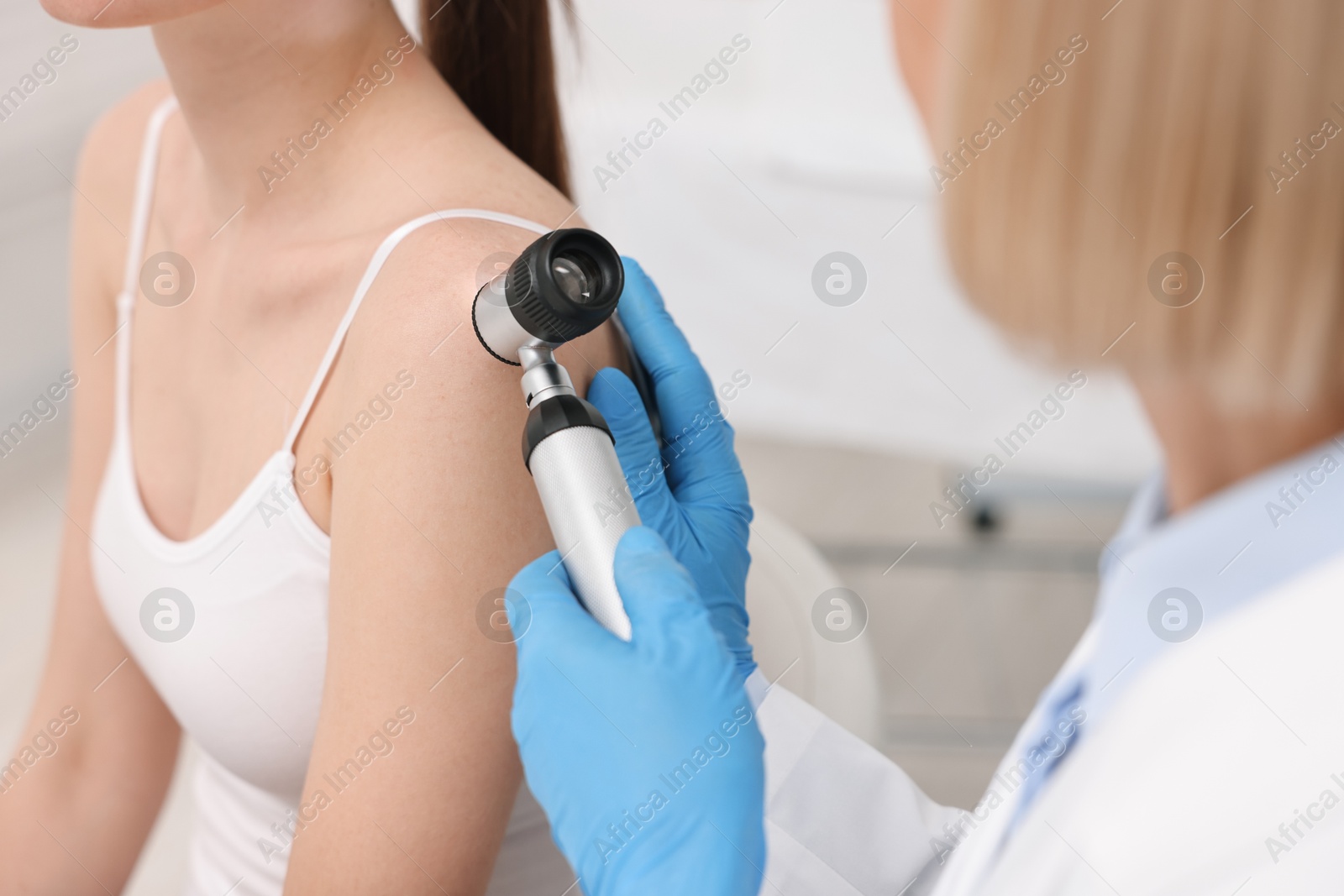 Photo of Dermatologist with dermatoscope examining patient in clinic, closeup