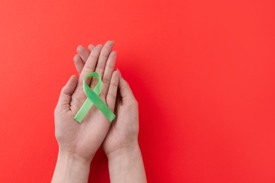 Woman with light green awareness ribbon on red background, top view. Space for text