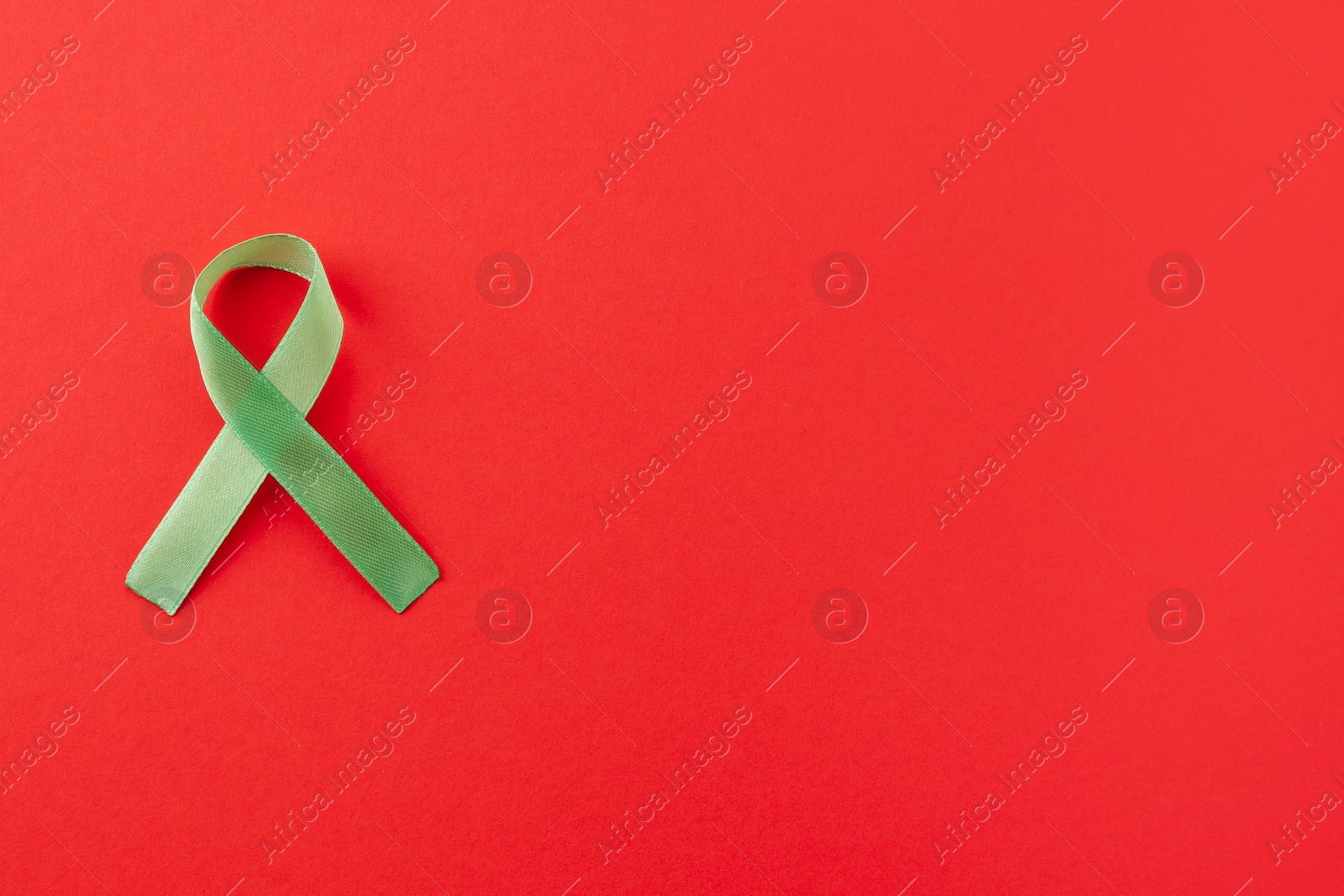 Photo of Light green awareness ribbon on red background, top view. Space for text