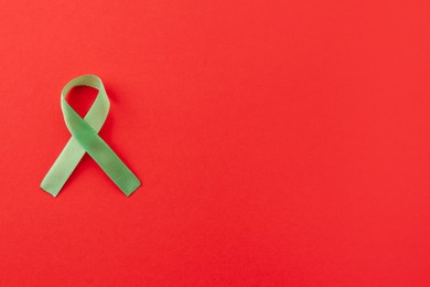 Light green awareness ribbon on red background, top view. Space for text