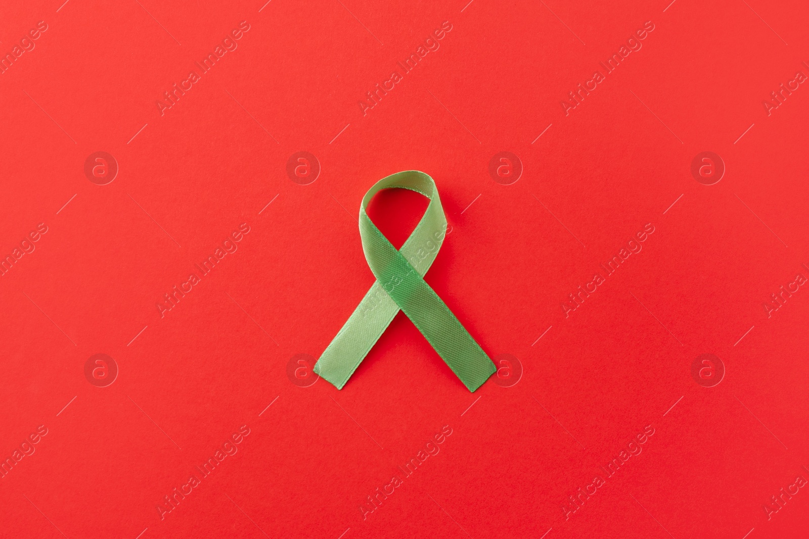 Photo of Light green awareness ribbon on red background, top view