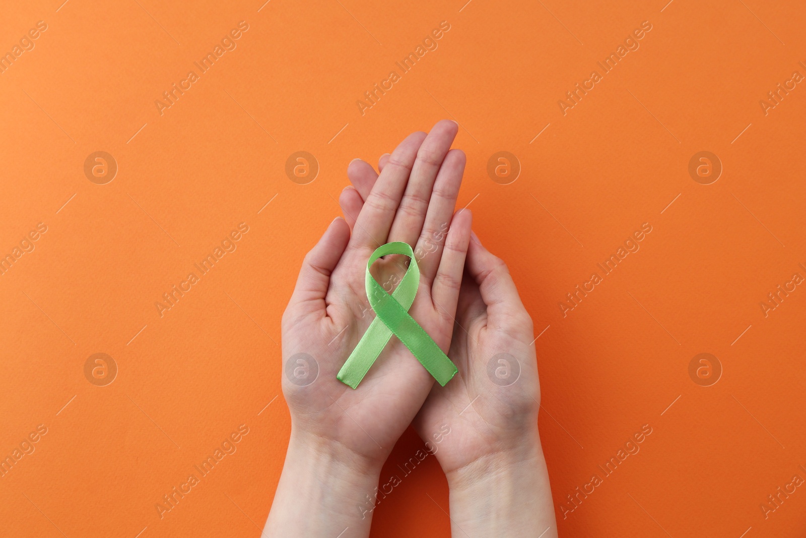 Photo of Woman with light green awareness ribbon on orange background, top view