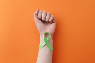 Photo of Woman with green awareness ribbon on orange background, top view