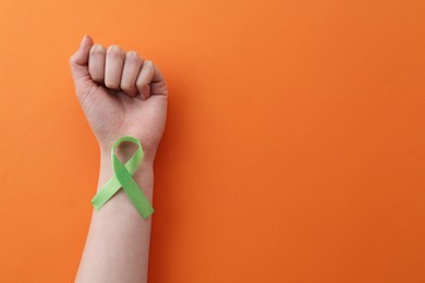 Woman with green awareness ribbon on orange background, top view. Space for text