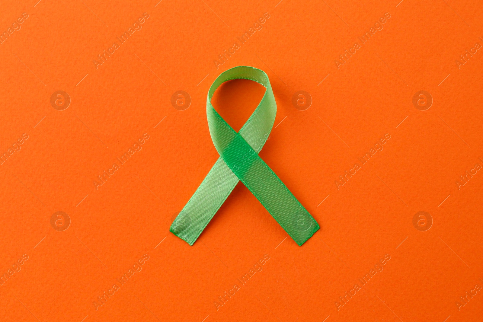 Photo of Light green awareness ribbon on orange background, top view