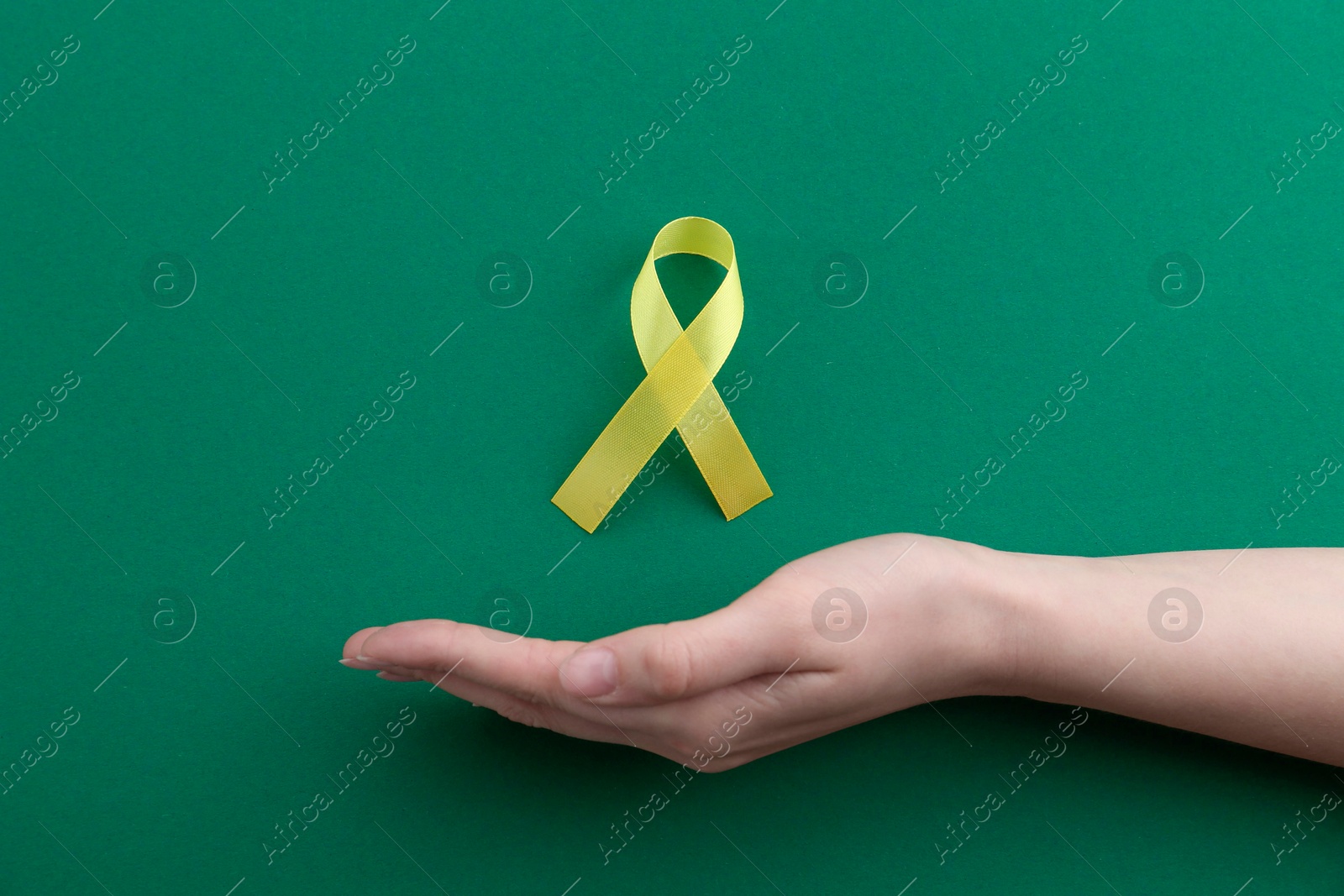 Photo of Woman with yellow awareness ribbon on green background, top view. Space for text