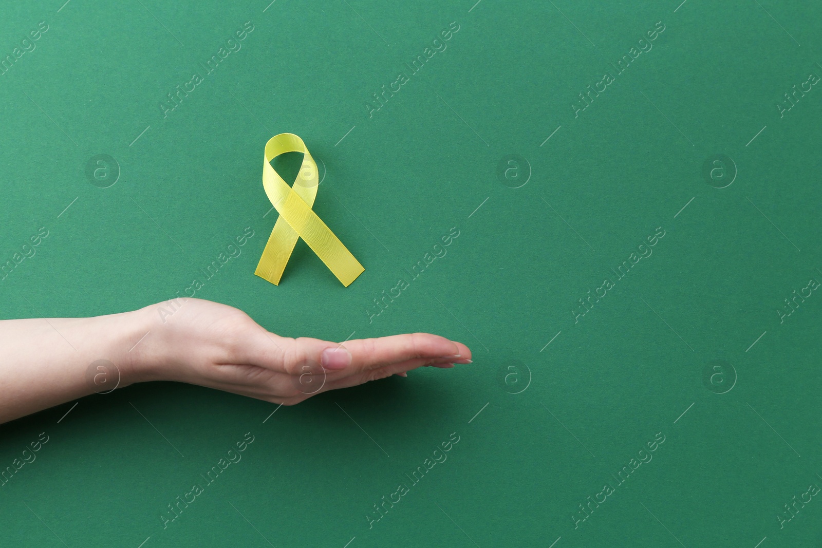 Photo of Woman with yellow awareness ribbon on green background, top view. Space for text