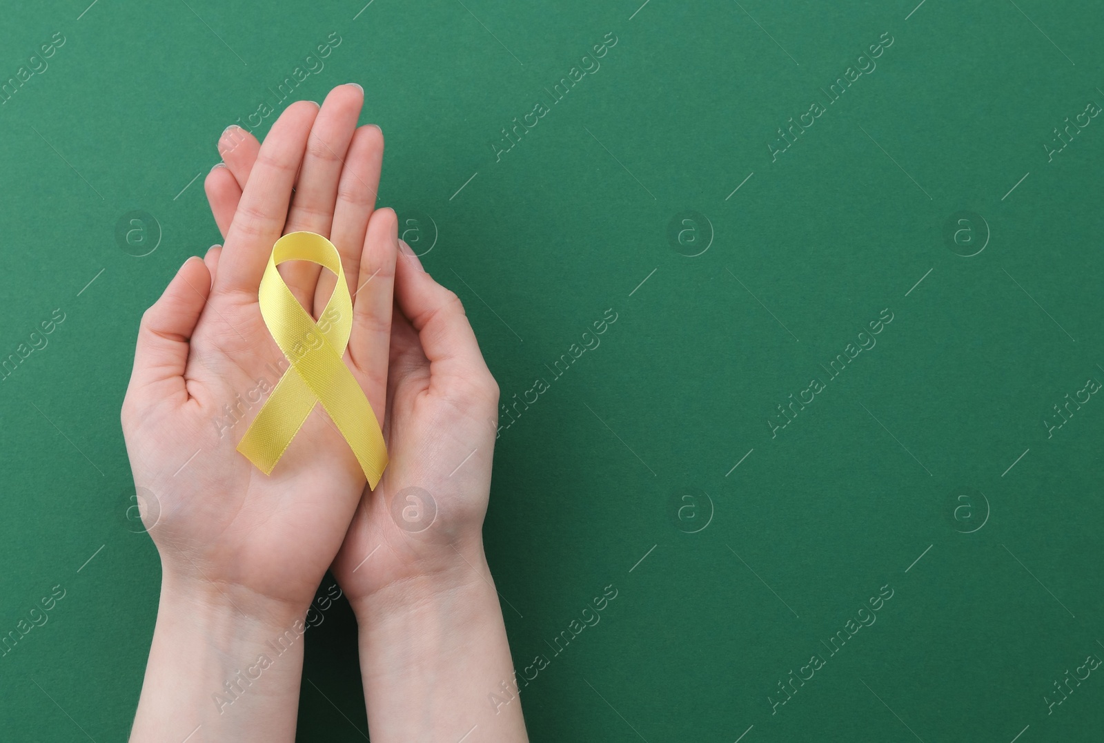 Photo of Woman with yellow awareness ribbon on green background, top view. Space for text