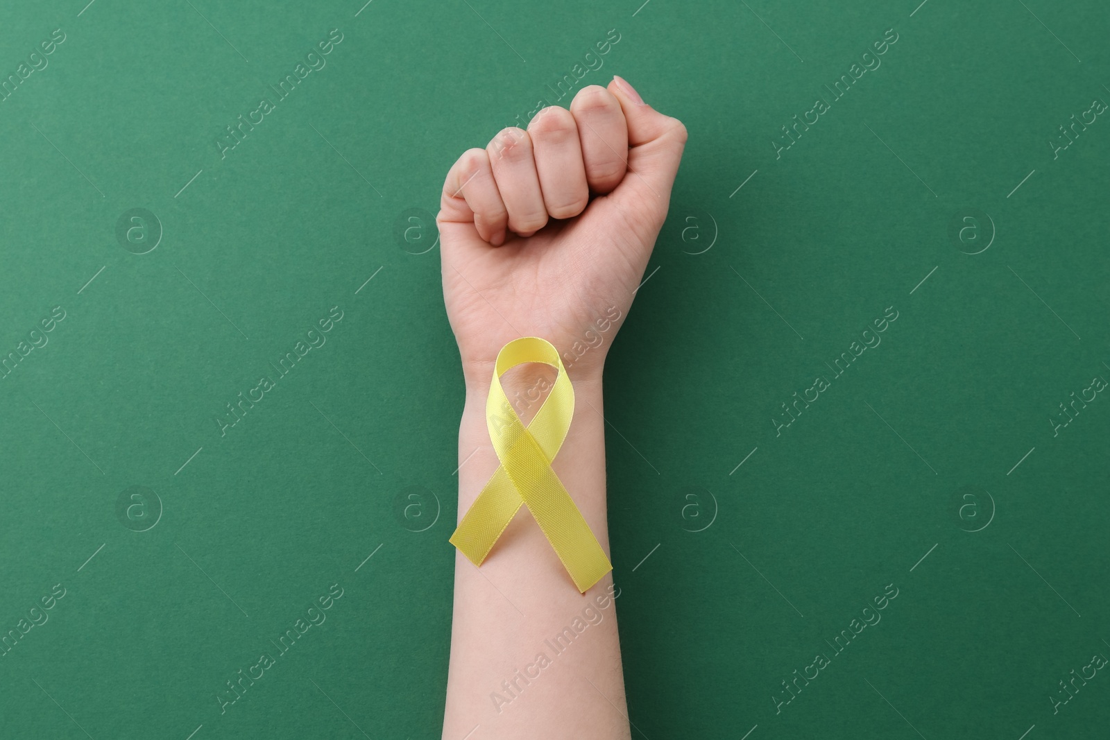 Photo of Woman with yellow awareness ribbon on green background, top view