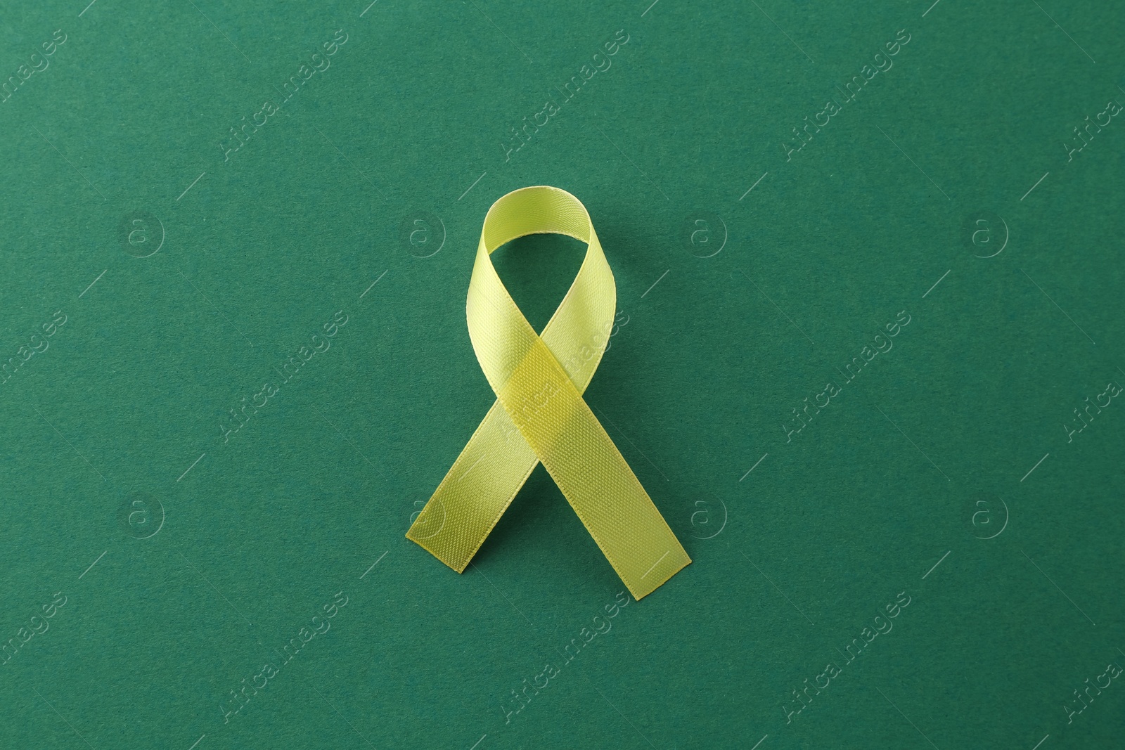 Photo of Yellow awareness ribbon on green background, top view