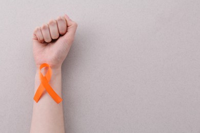 Photo of Woman with orange awareness ribbon on gray background, top view. Space for text