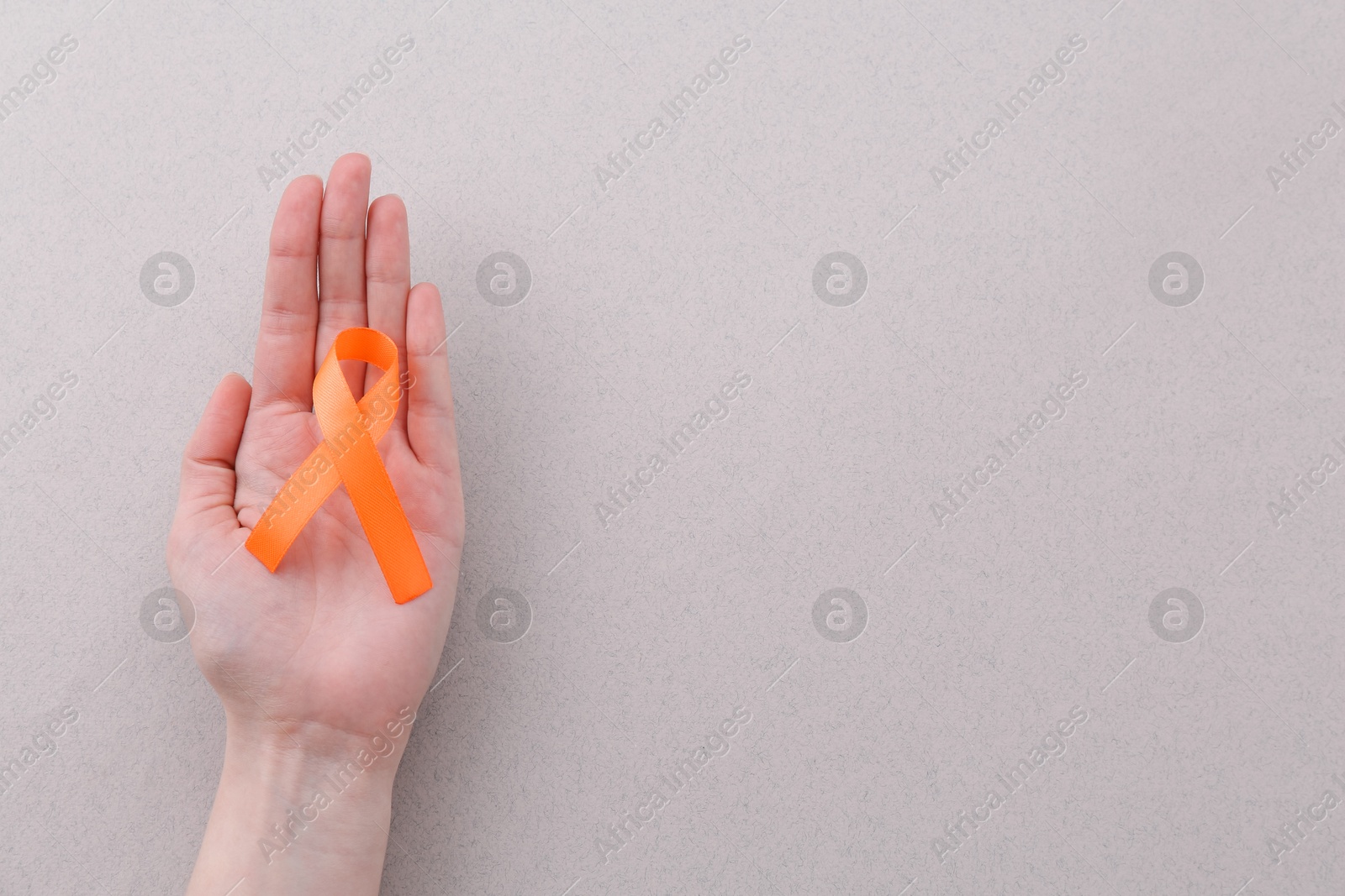 Photo of Woman with orange awareness ribbon on gray background, top view. Space for text