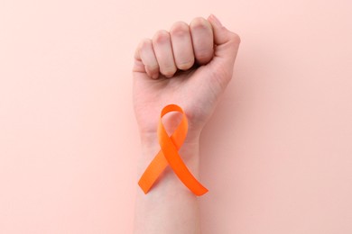 Woman with orange awareness ribbon on beige background, top view