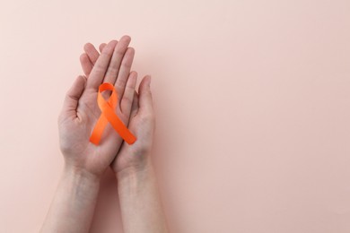 Photo of Woman with orange awareness ribbon on beige background, top view. Space for text